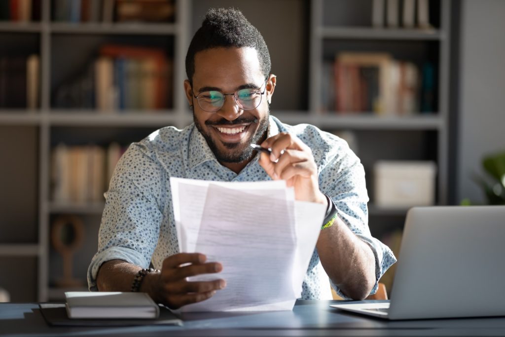 Man with glasses smiling while reading tax refund paperwork